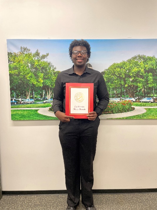 Intern Christian Okafor holds a framed copy of a Senate Resolution and poses for a photo. 